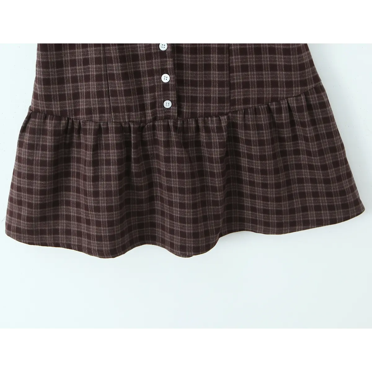 Close-up of the ruffled skirt hem, showing the brown plaid pattern and front button placket.