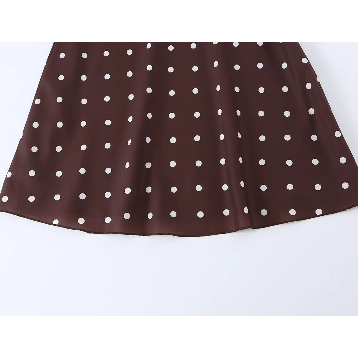 Close-up of the skirt hem of brown polka dot dress, showing flowy fabric and finished edge design.
