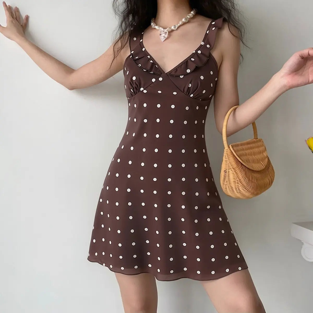  Model wearing brown polka dot mini dress with a rattan bag, showing casual everyday styling and flattering fit.