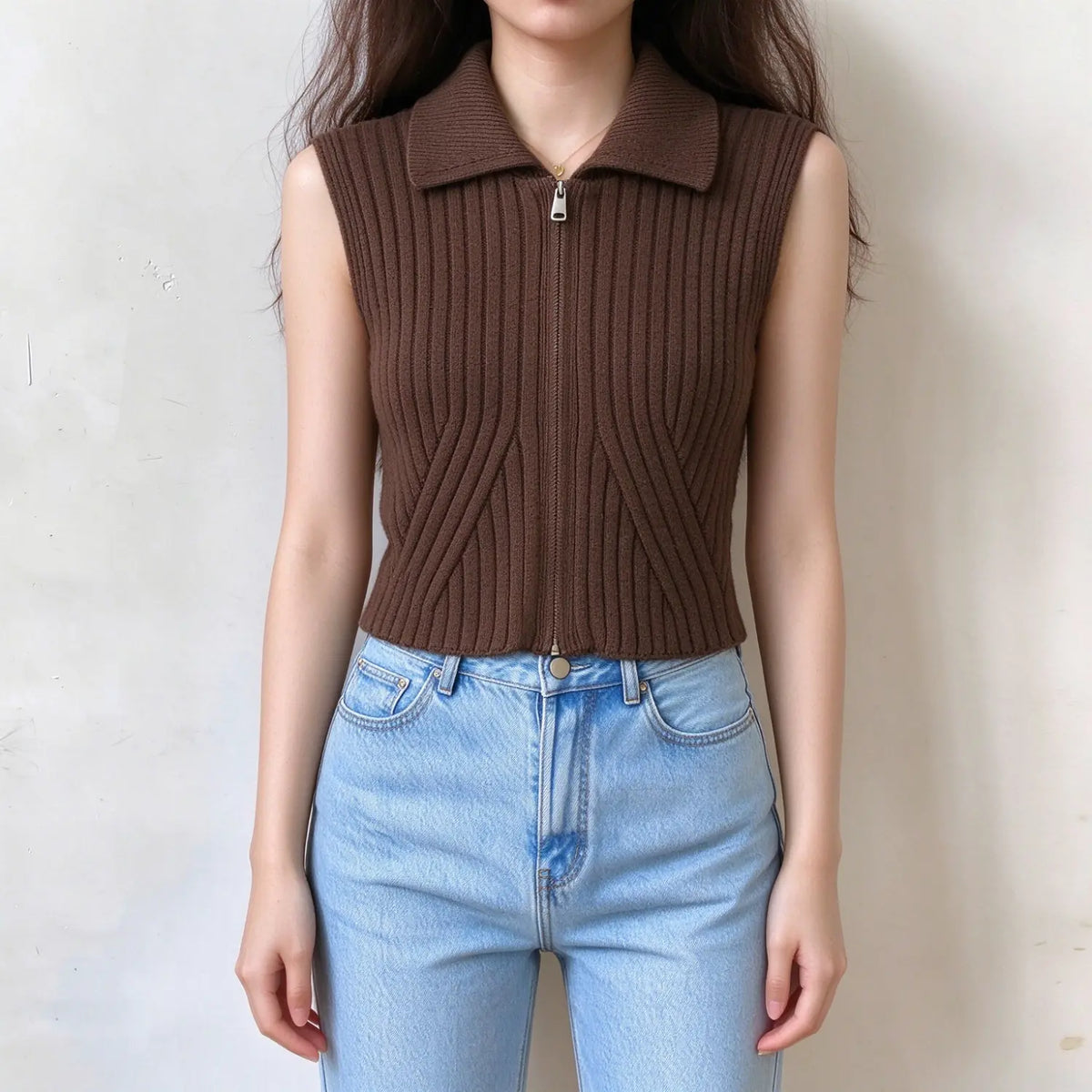 Model wearing brown ribbed knit sleeveless vest with lapel collar and full front zipper, cropped fitted style, paired with light blue jeans, front view