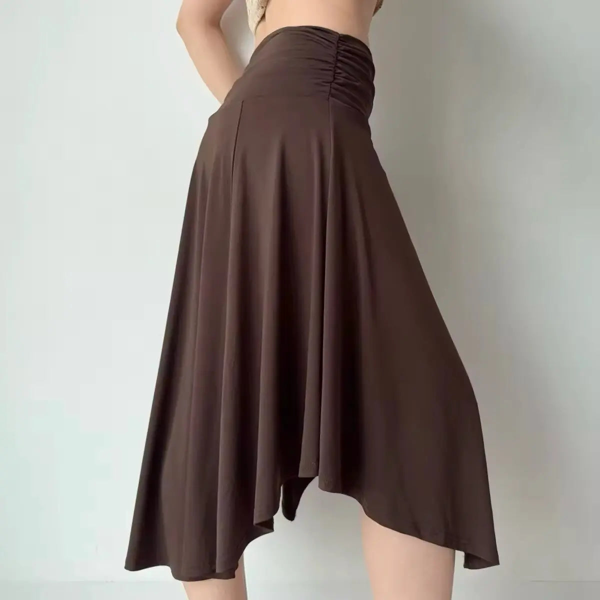 Side view of a brown asymmetrical midi skirt with a ruched waistband, highlighting the soft drape of the fabric and uneven hem.