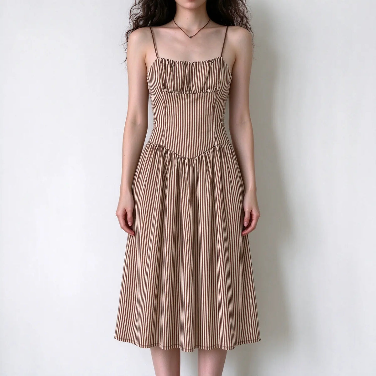 Female model front view wearing brown and beige striped spaghetti strap midi dress, square neck, fitted waist, flowy long A-line skirt