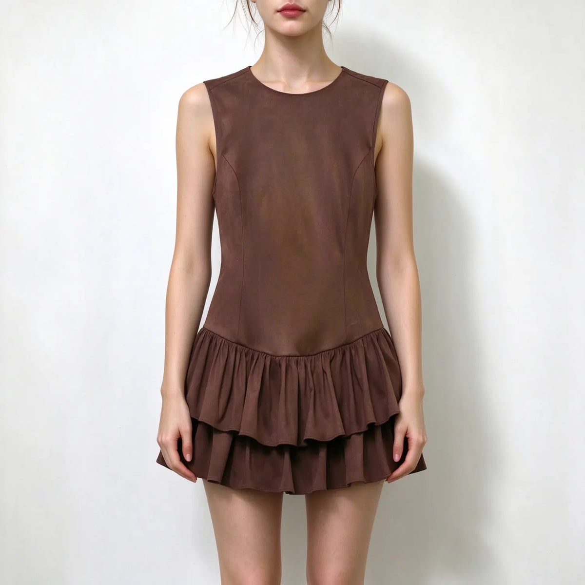 Model wearing brown suede sleeveless round neck mini dress with double tier ruffle hem, plain white background