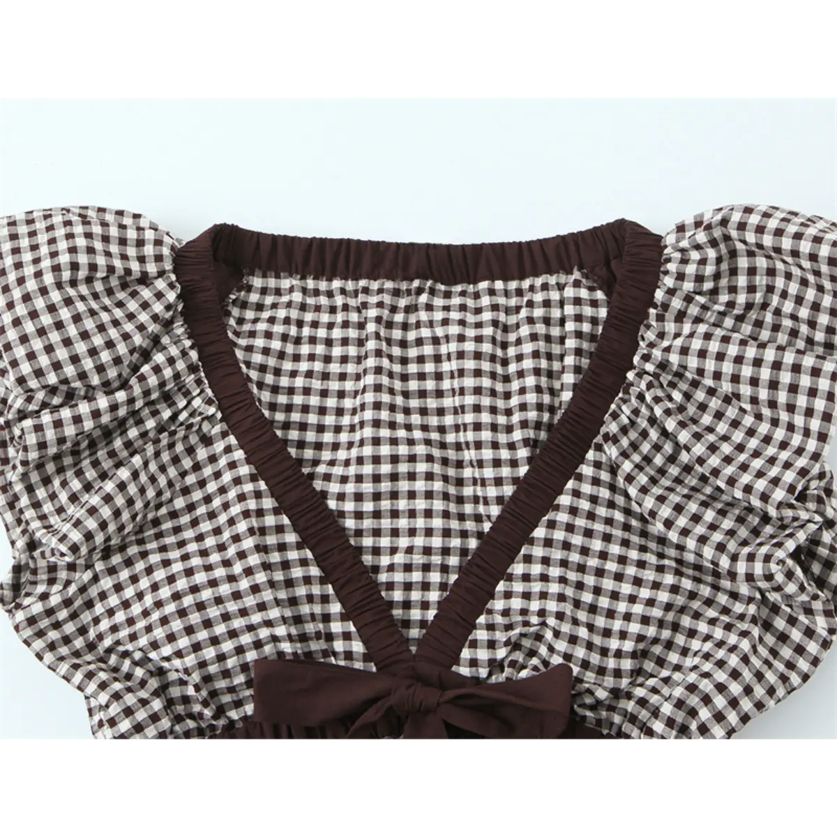 Front view of the gingham top, showing the V-neckline, brown elasticated trim, and center bow detail