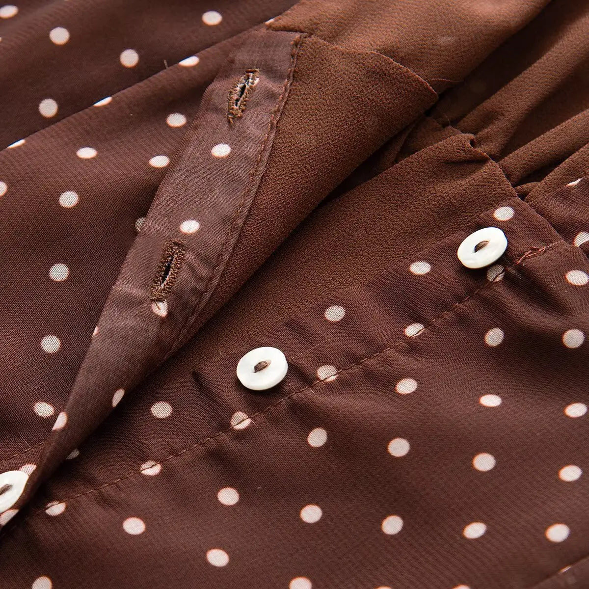  Close-up detail of the mother-of-pearl button placket and buttonholes on a brown and white polka dot chiffon dress.