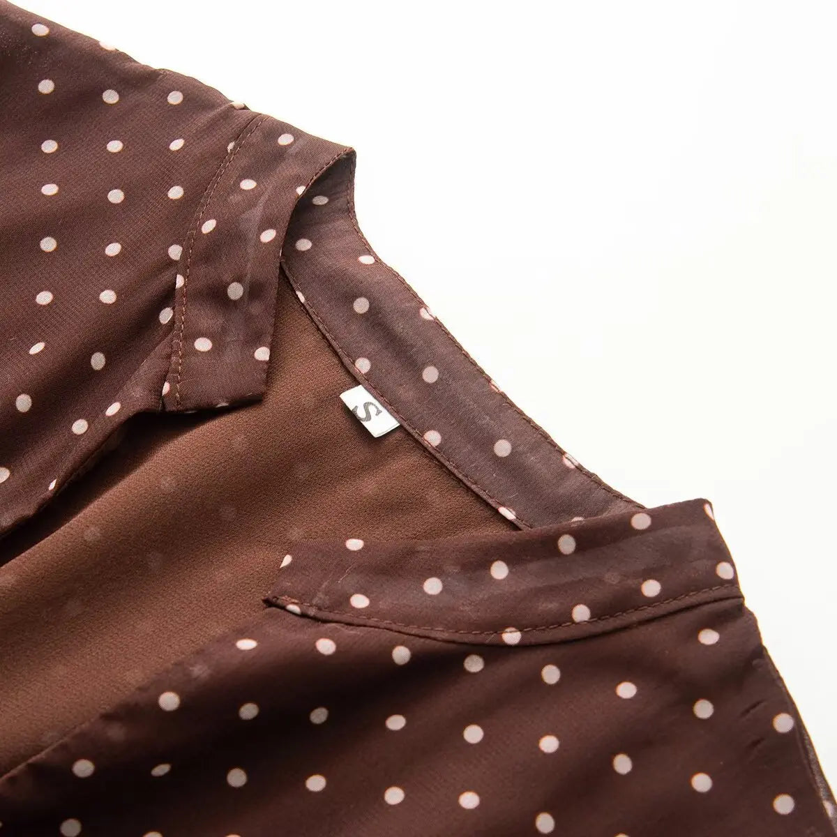 Close-up detail of the notched V-neck collar and inner size label on a brown and white polka dot chiffon dress.