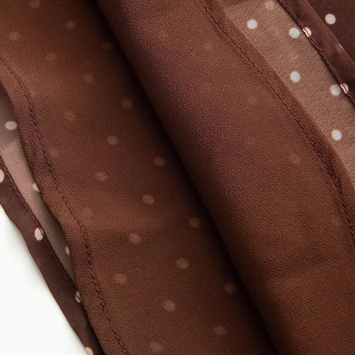 Close-up detail of the lightweight chiffon fabric on a brown and white polka dot dress, showing the pattern and seam construction.