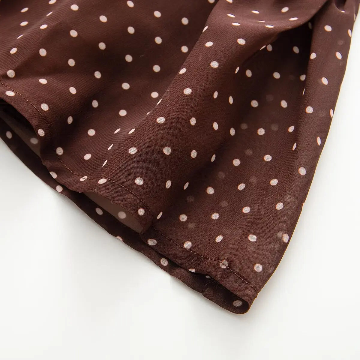 Close-up detail of the gathered waist construction on a brown and white polka dot chiffon dress.