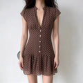 Model wearing a brown and white polka dot chiffon mini dress with a notched V-neck, button placket, and ruffled hem, front view.