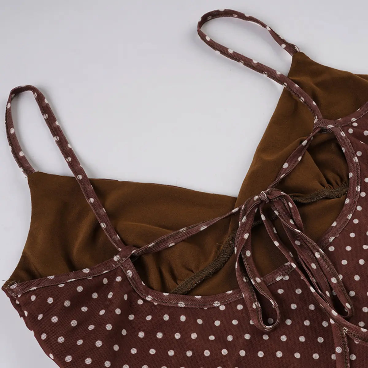Close-up view of the back bust area of a brown mesh dress with white polka dots, showing the tie closures and inner lining.

