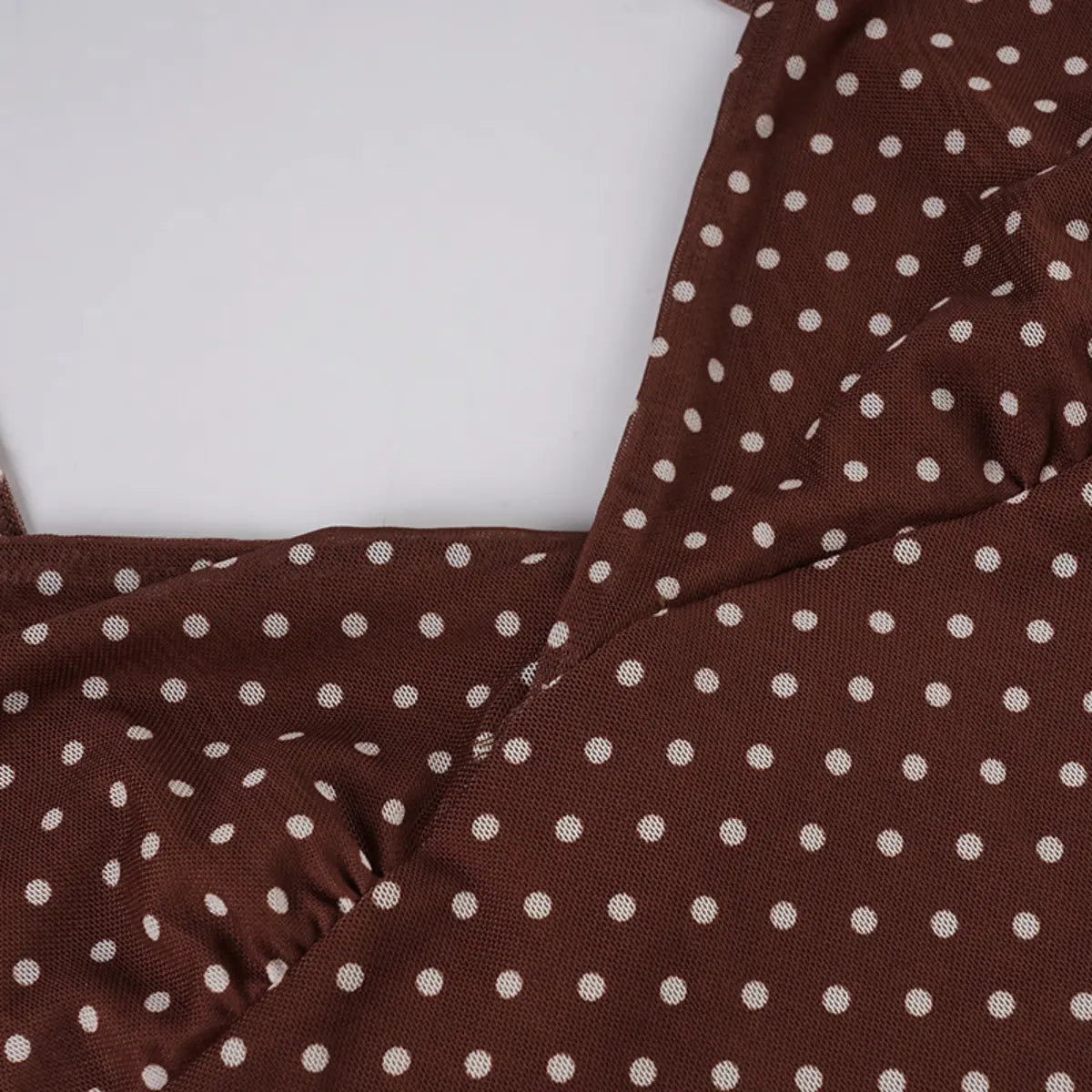 Close-up view of the bust area of a brown mesh dress with white polka dots, showing the gathered fabric and sheer texture.