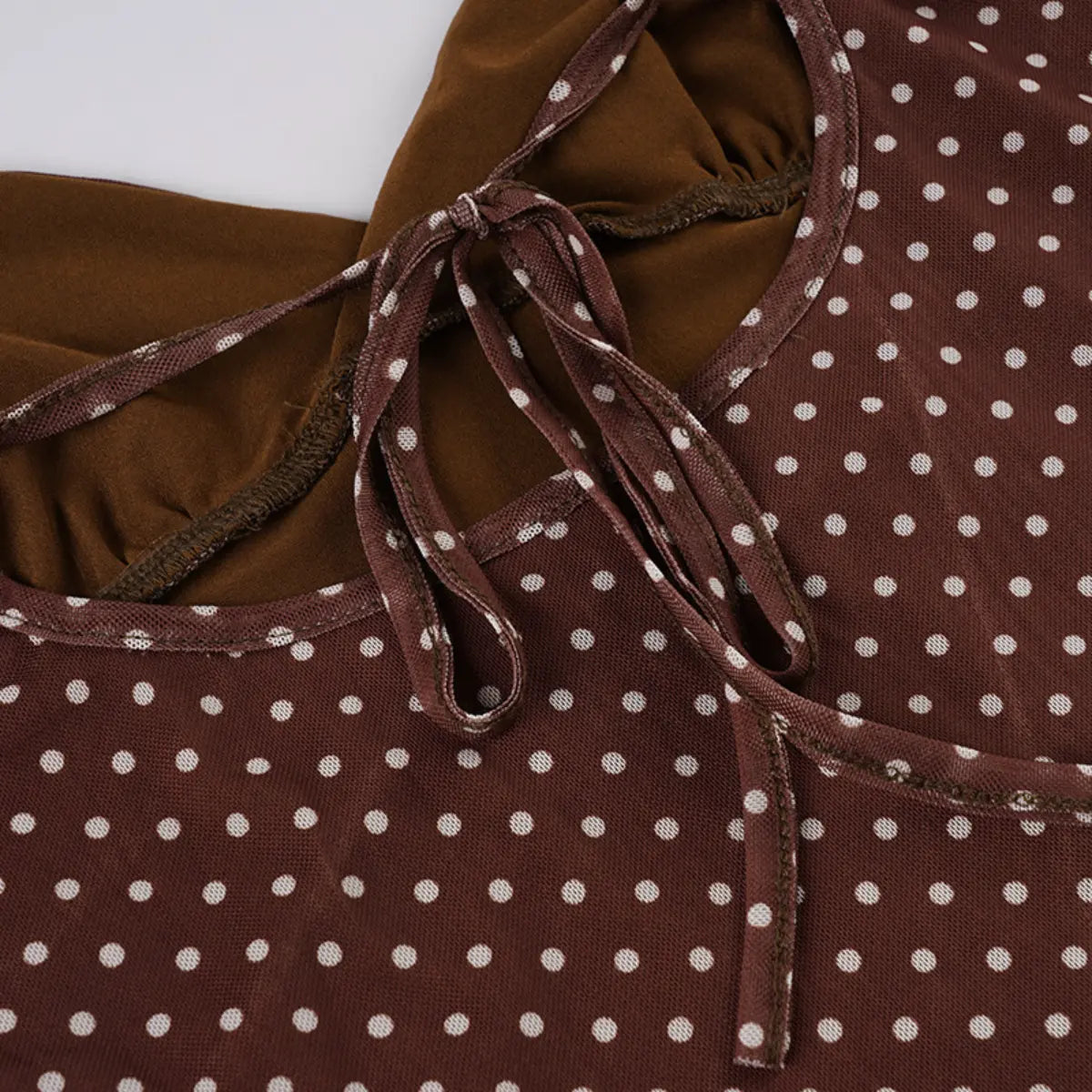 Close-up view of the bust area of a brown mesh dress with white polka dots, showing the tie closure and gathered fabric detail.