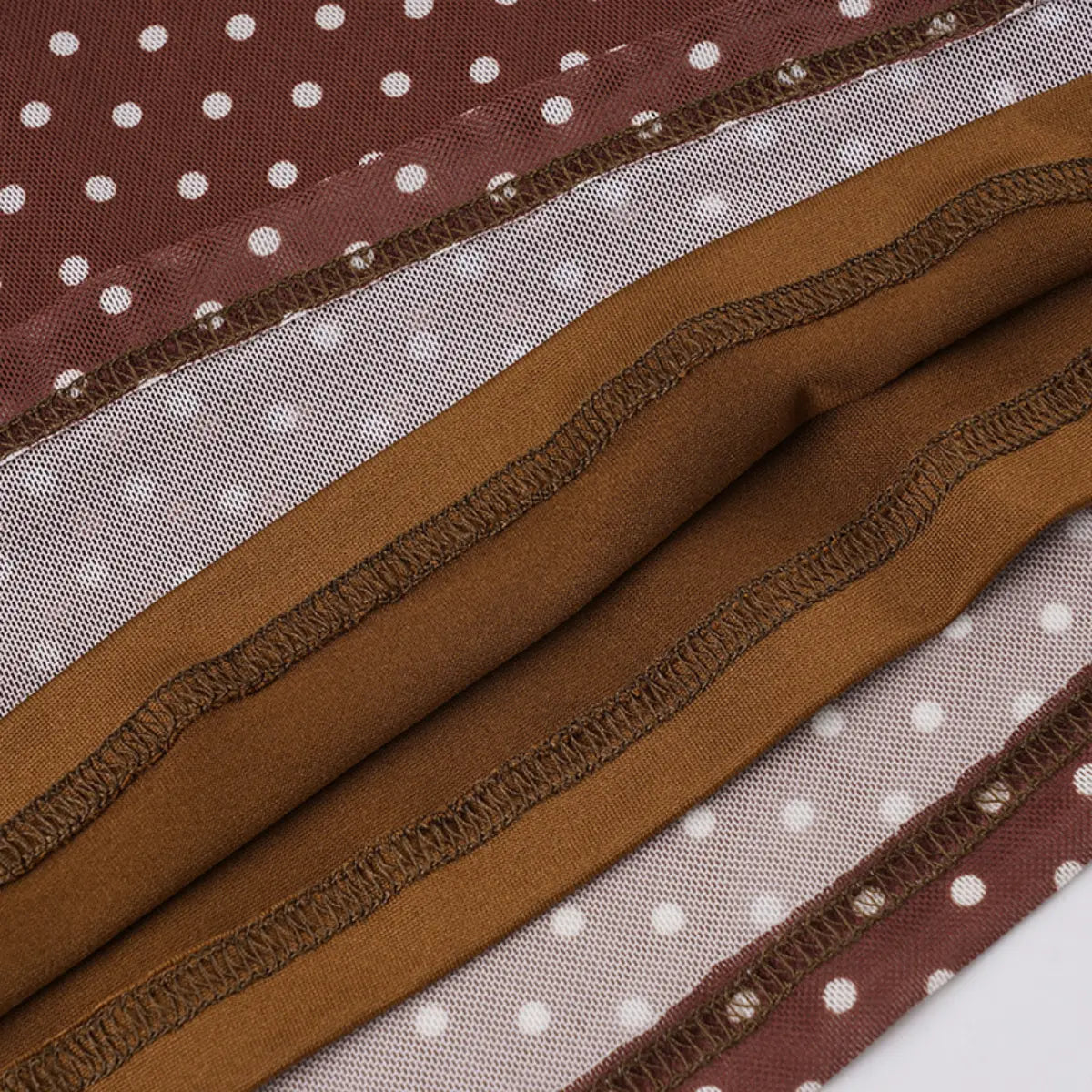 Close-up view of the dress hem, showing the contrast between the brown polka-dot mesh outer layer and the solid brown lining, plus the finished stitching.