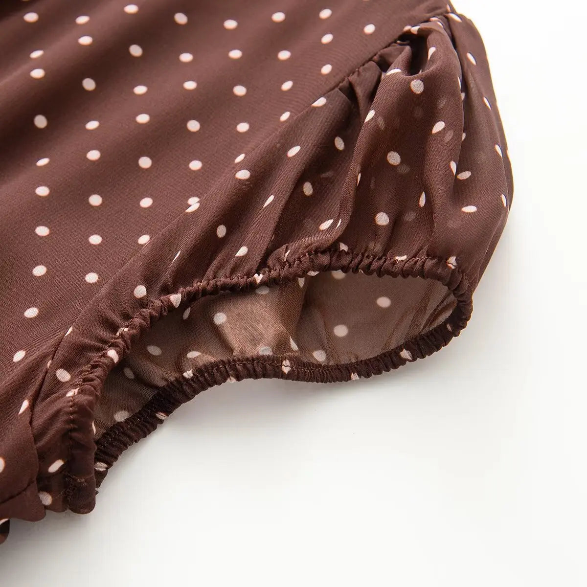 Close-up detail of the ruffled elasticated cap sleeve on a brown and white polka dot chiffon dress, showing the gathered fabric and sheer texture.