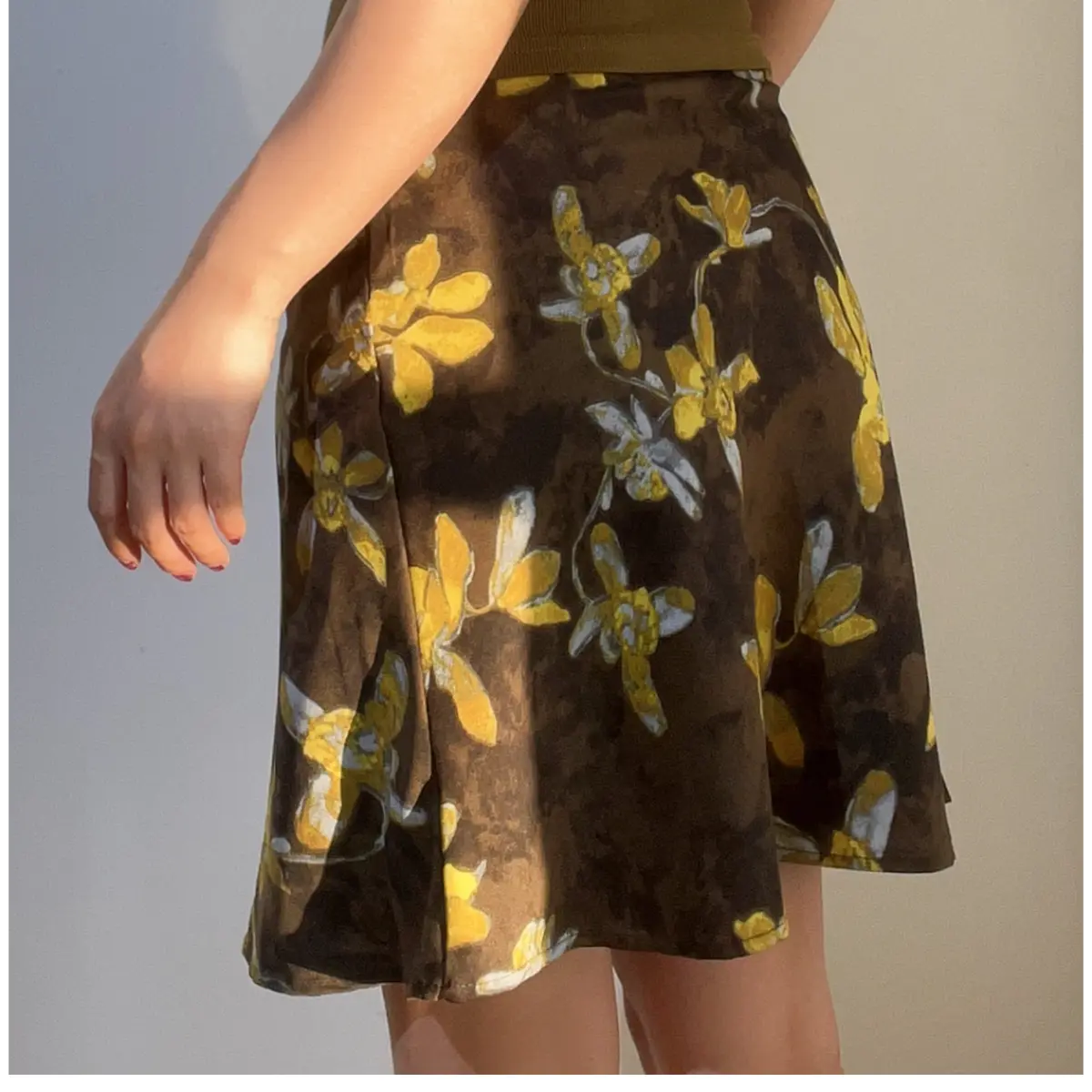 Side view of a brown and yellow floral chiffon mini skirt, showing the print and flowy silhouette, paired with an olive green ribbed camisole.
