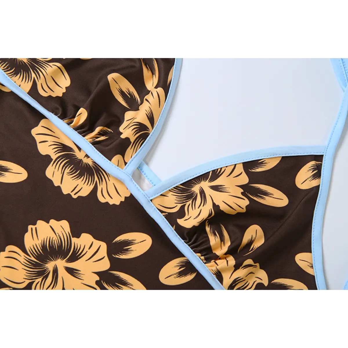 Close-up view of the bust area of a brown halter dress with yellow hibiscus print, showing the light blue contrast trim and stitching.