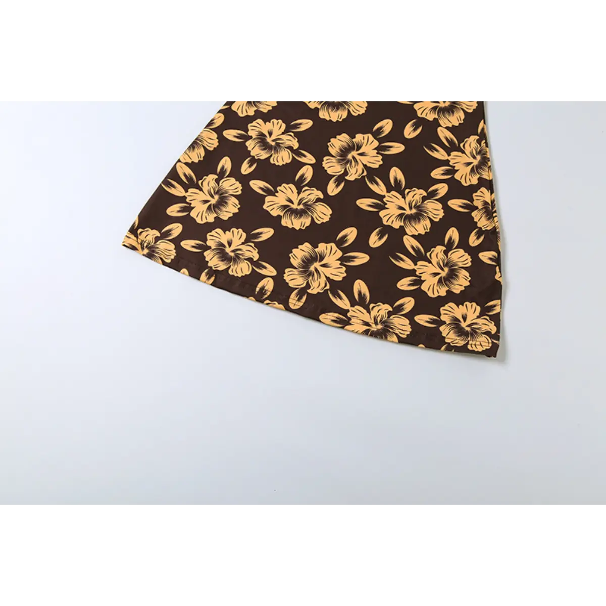 Close-up of the flared skirt hem of a brown halter dress with yellow hibiscus floral print, laid flat.