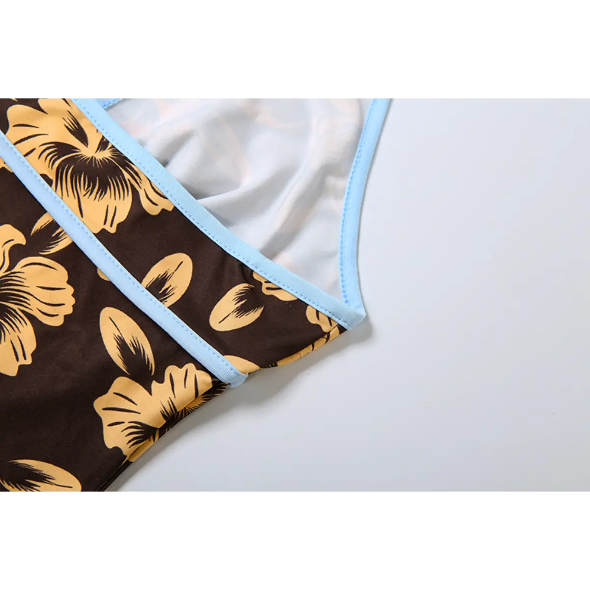 Close-up view of the light blue contrast trim on a brown halter dress with yellow hibiscus print, showing the clean stitching and inner lining.