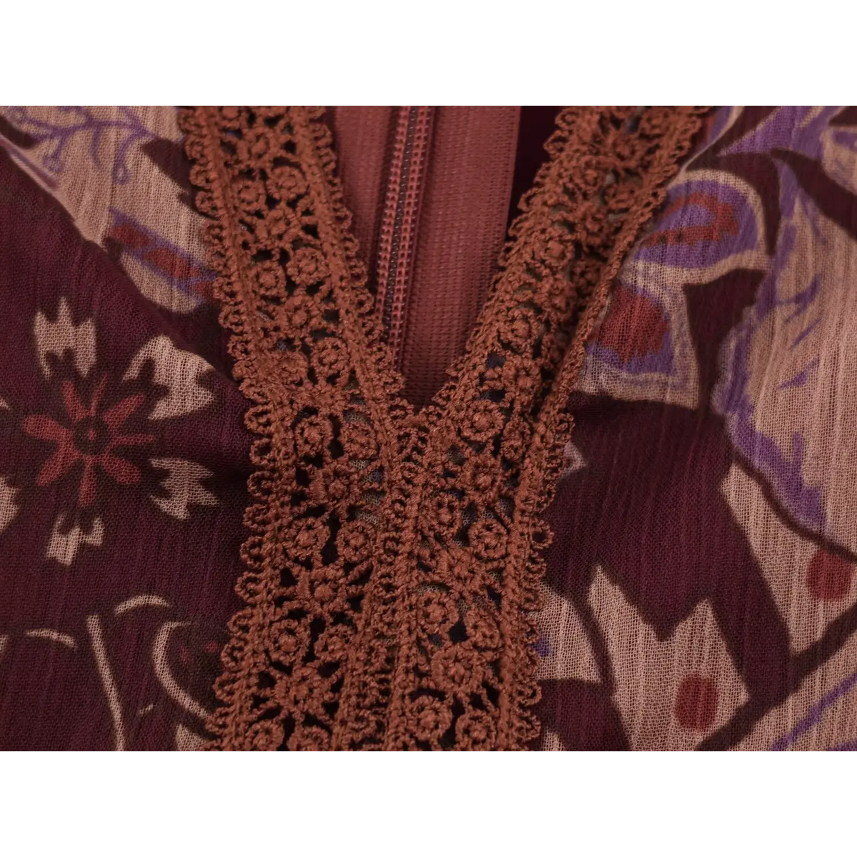 Macro shot of textured crochet lace trim embellishing burgundy maxi dress neckline
