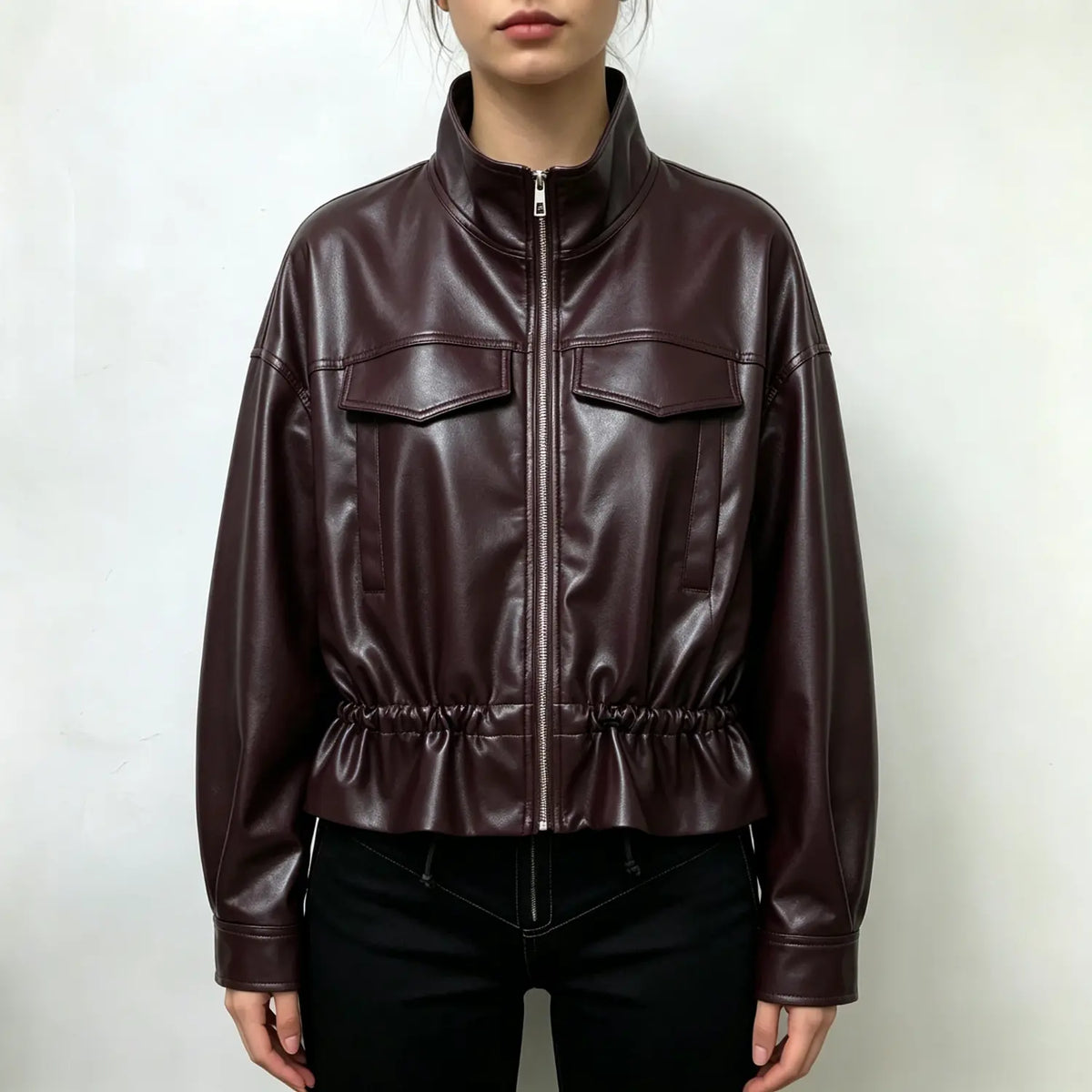 Model wearing burgundy faux leather cropped jacket, stand collar, front zipper, flap pockets and drawstring hem