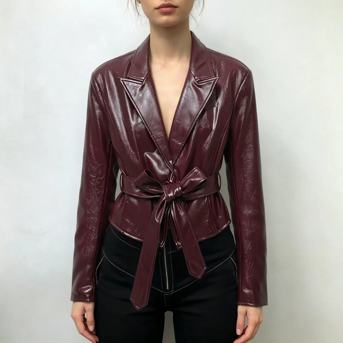 Model wearing burgundy leather look blazer with self tie belt and black trousers