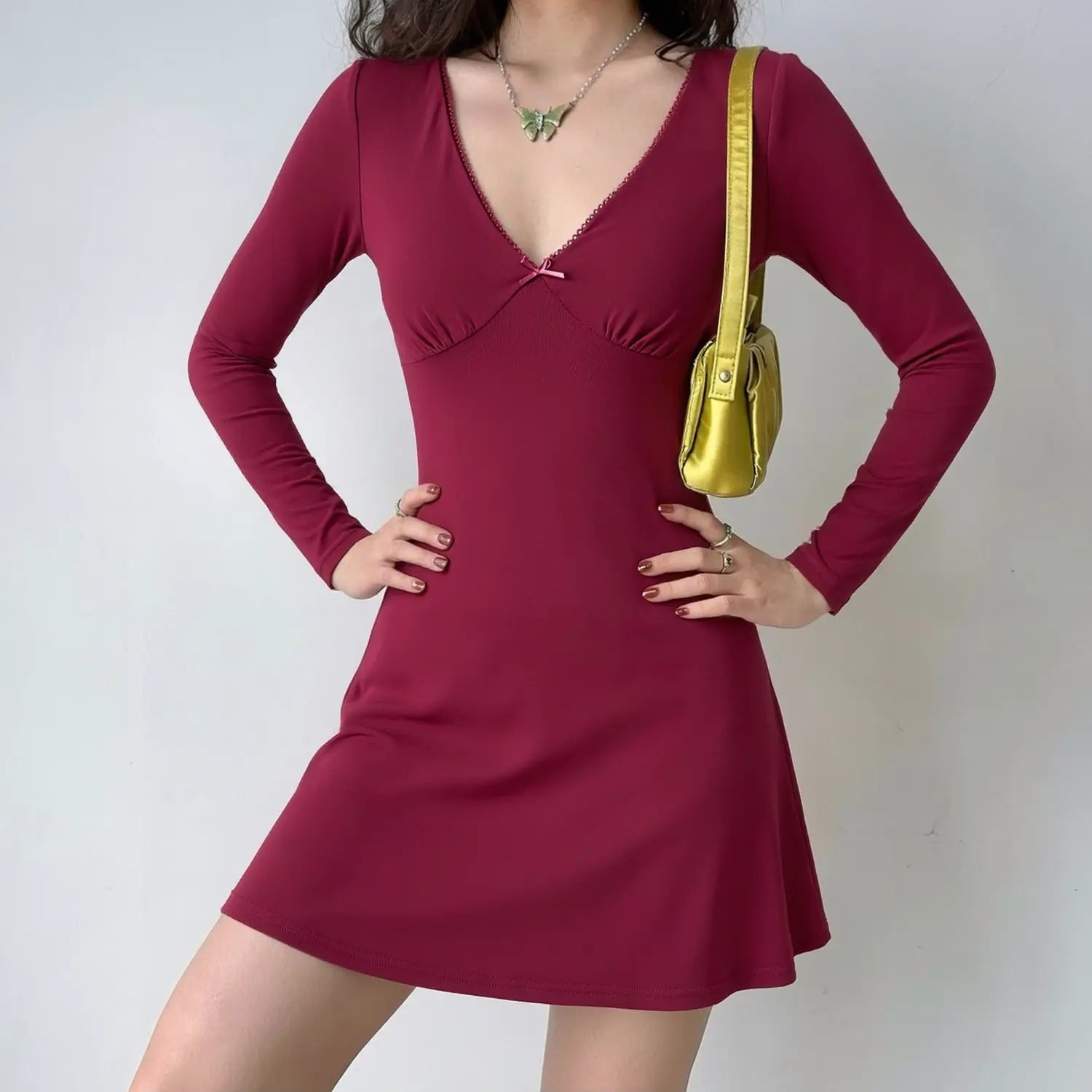 Burgundy long sleeve deep v neck mini dress on female model, tiny front bow, fitted waist and flared skirt, party outfit