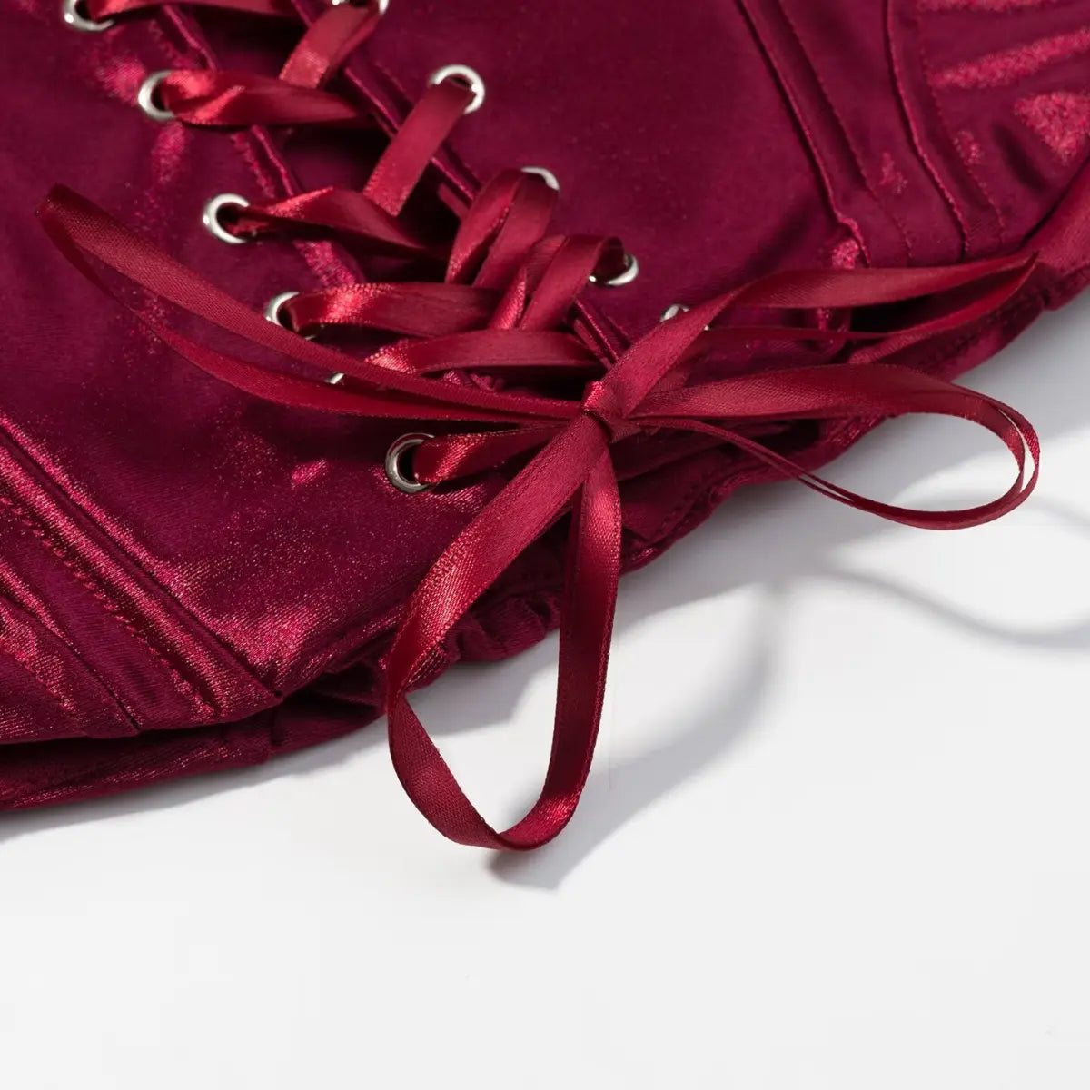 Close-up of the satin ribbon tie at the bottom of the lace-up front on the burgundy corset top
