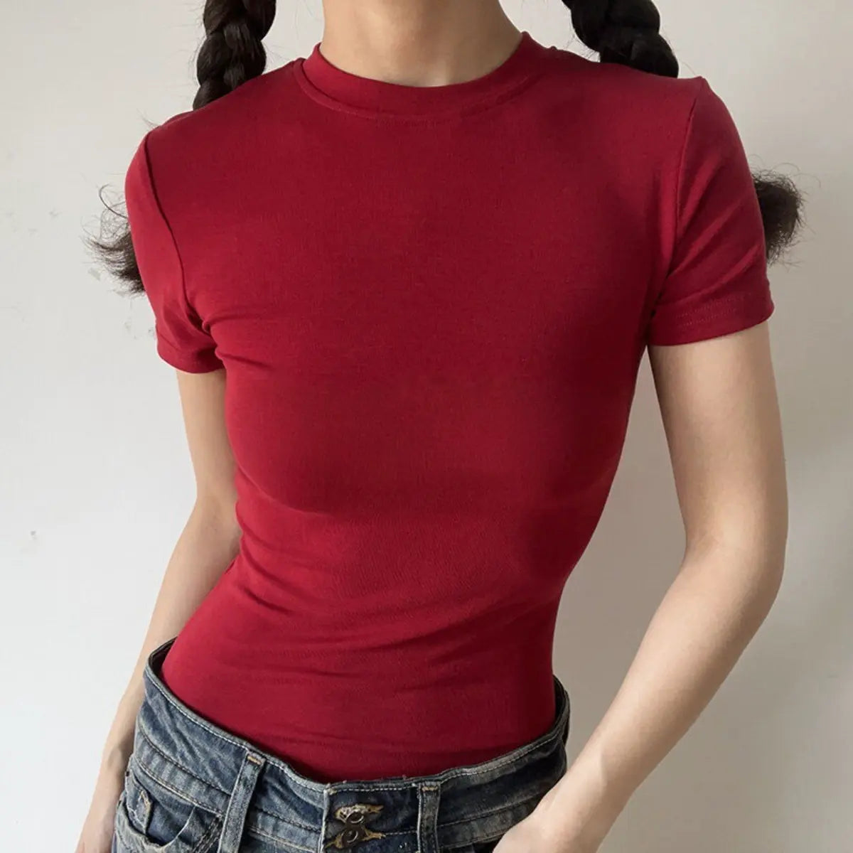 Lifestyle shot of form-fitting burgundy red ribbed crew-neck t-shirt, tucked into jeans