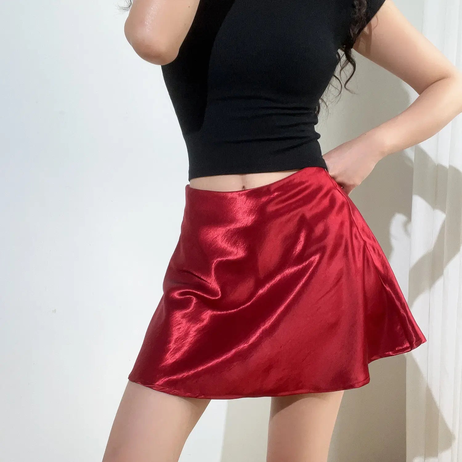 Female model wearing burgundy glossy satin high waist A-line mini skirt with black cropped top