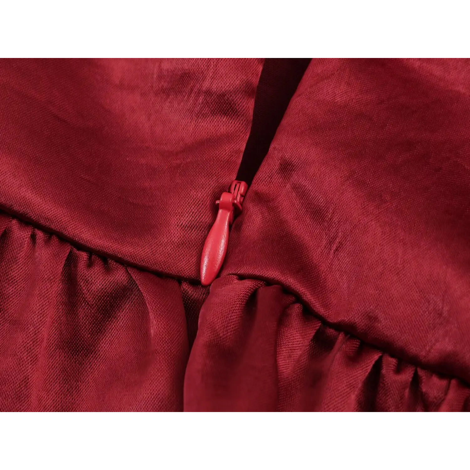  Macro shot of matching burgundy coated invisible zipper, teardrop fabric pull tab, waist horizontal gathering seam dividing bodice and flared skirt, shiny satin texture