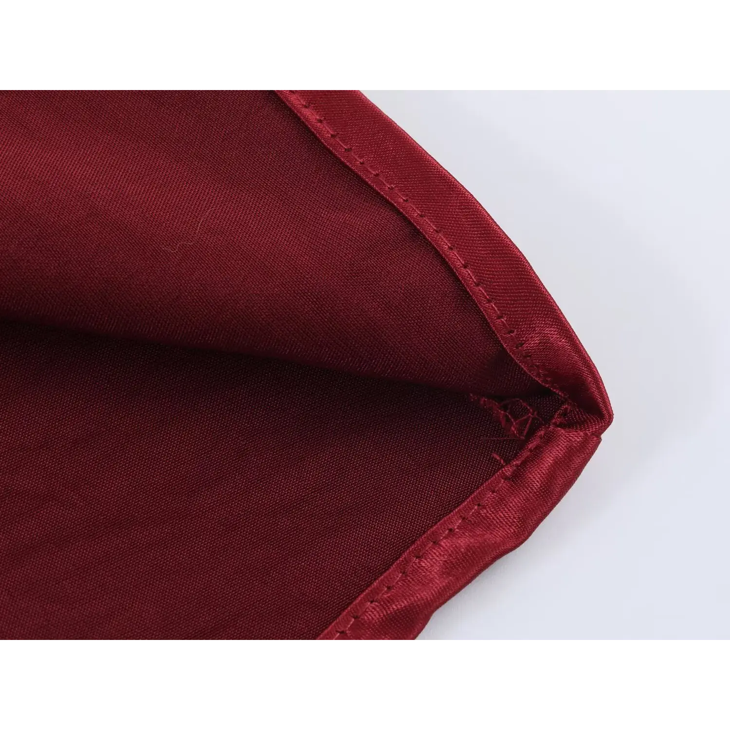 Close-up of skirt hem, uniform straight lockstitch binding edge, wrinkled glossy wine red satin fabric, neat finished hem craftsmanship