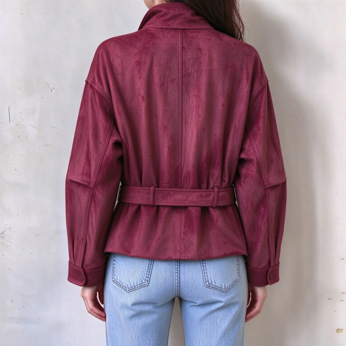 Back view of female model in burgundy faux suede belted jacket, vertical stitching details, matching back waist belt, long sleeve back silhouette