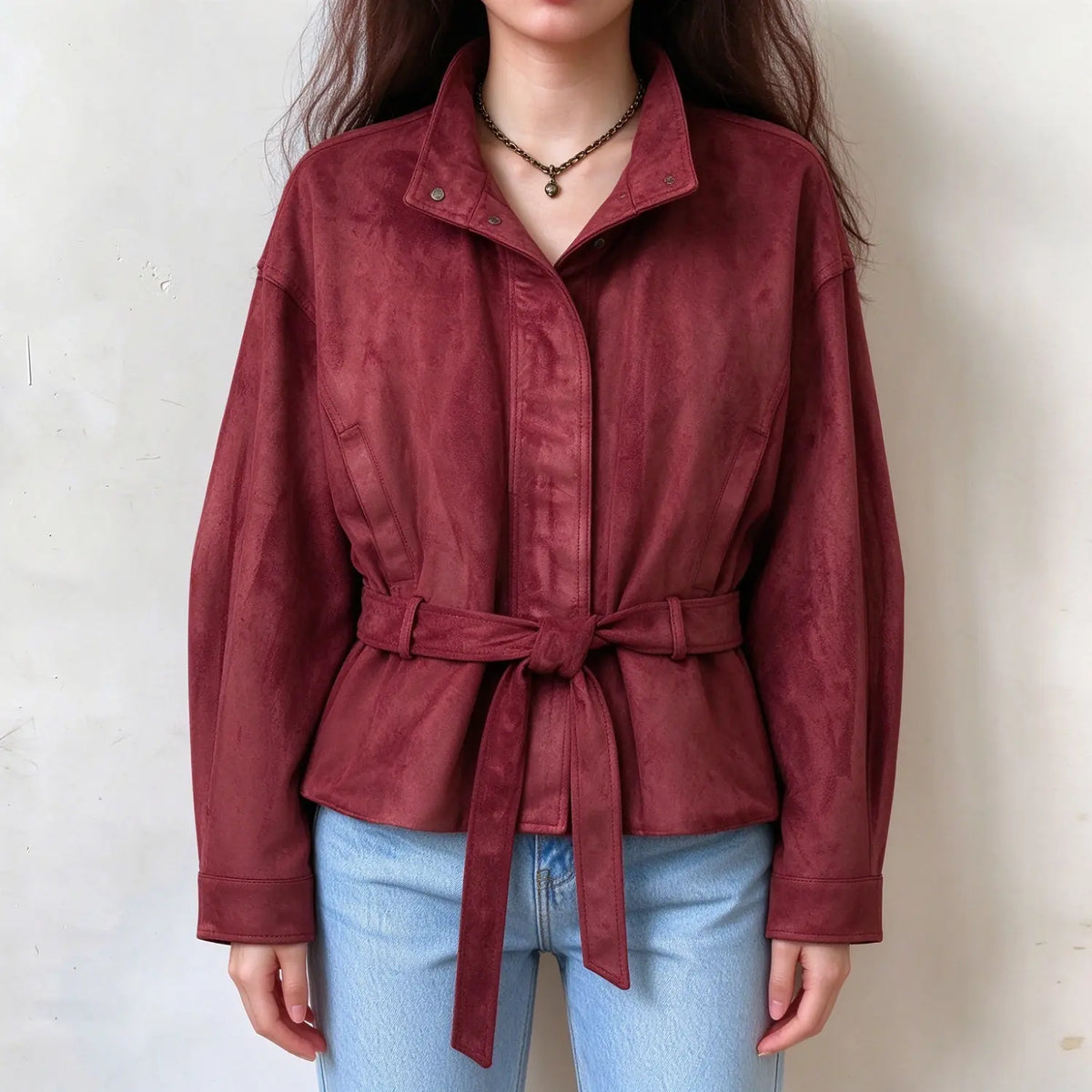 Female model wears burgundy faux suede belted jacket, stand collar with metal snap buttons, long sleeve, self tie waist belt, front full torso shot