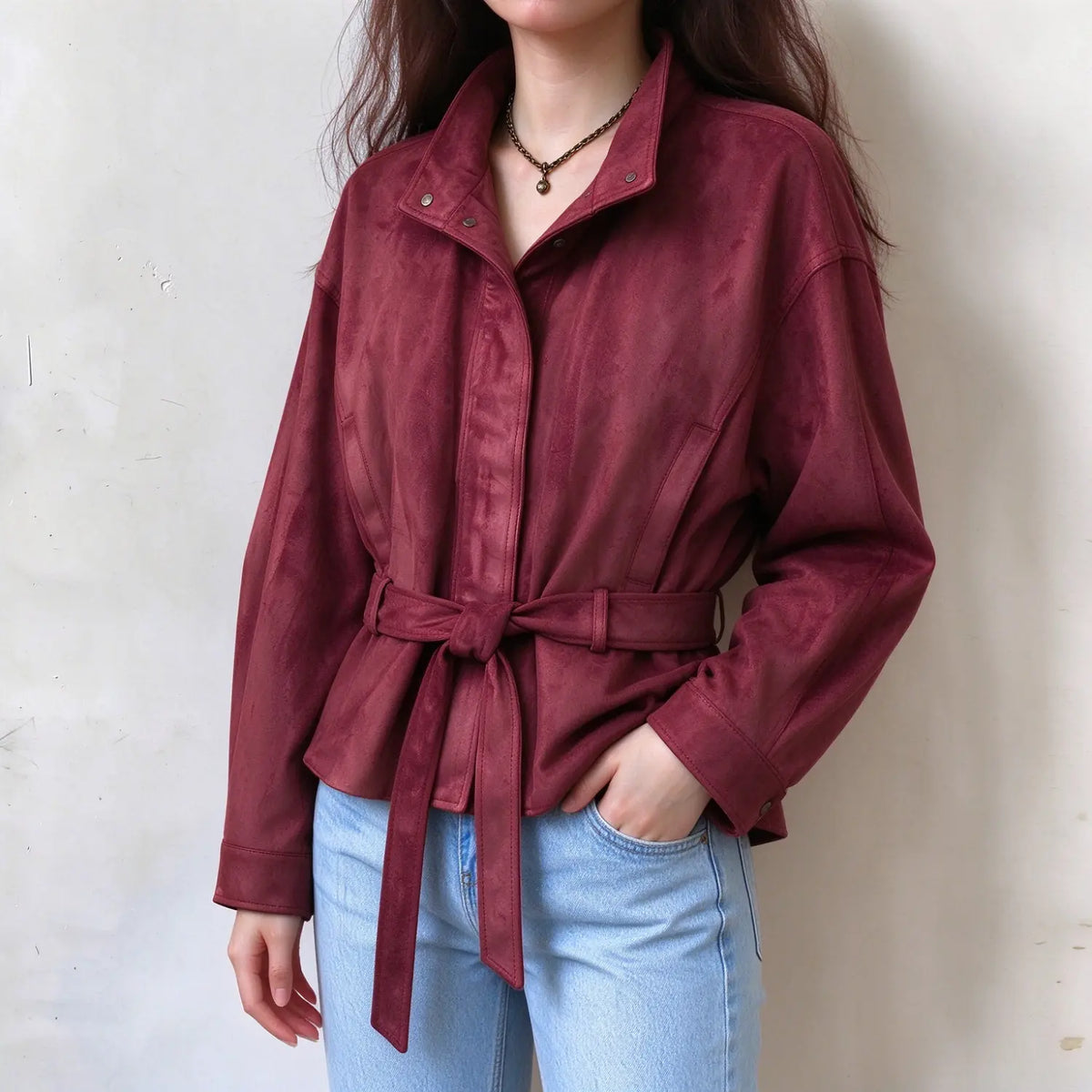 Female model in wine red faux suede jacket, adjustable waist tie belt, stand collar design, one hand resting in jeans pocket, casual wearing display
