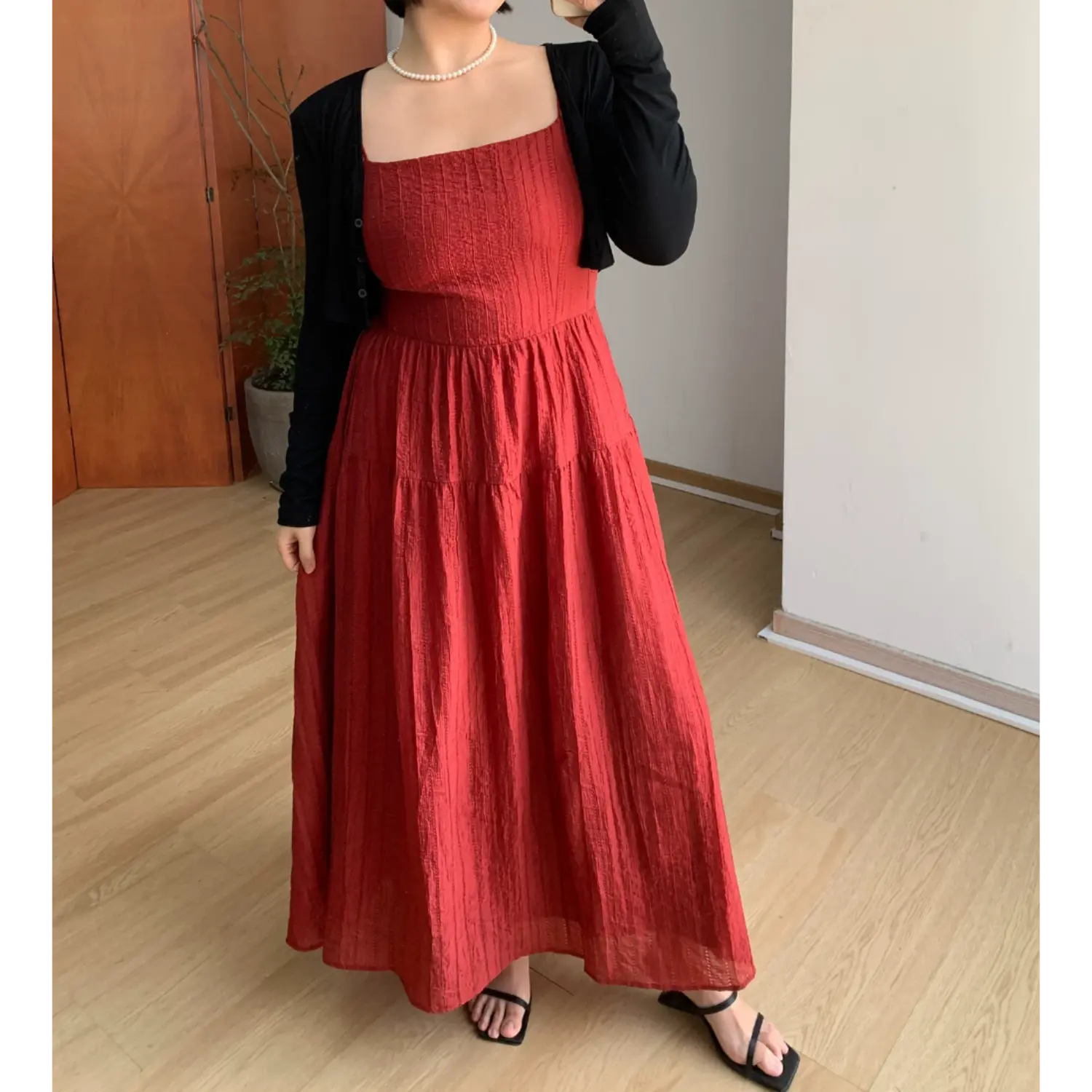 Full body indoor mirror shot of deep red crinkled textured tiered maxi dress, layered slim black long sleeve cropped knit cardigan, matching black square slide sandals