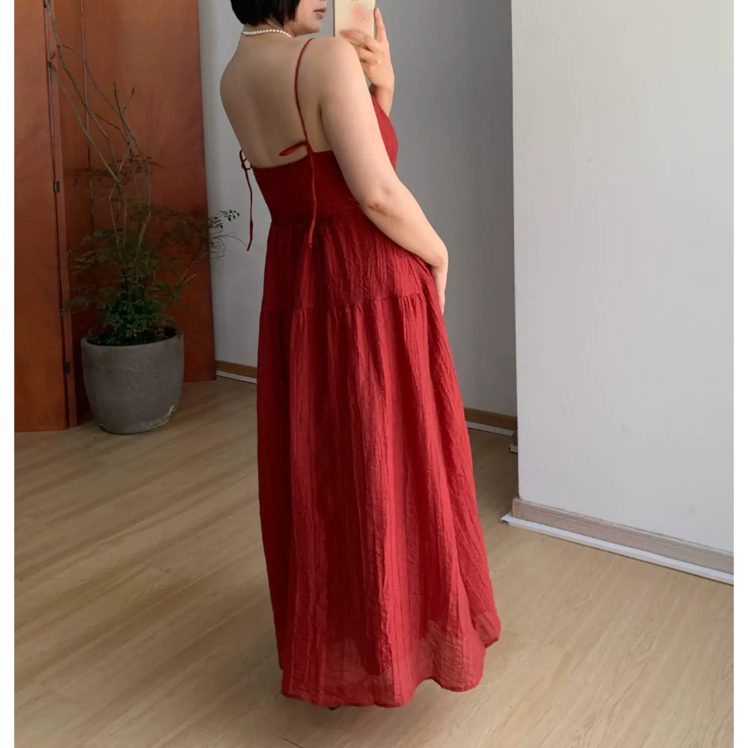 Three-quarter back indoor mirror shot of burgundy textured tier maxi slip dress, self-fabric tie closure on rear bust, thin adjustable spaghetti straps and sheer layered skirt