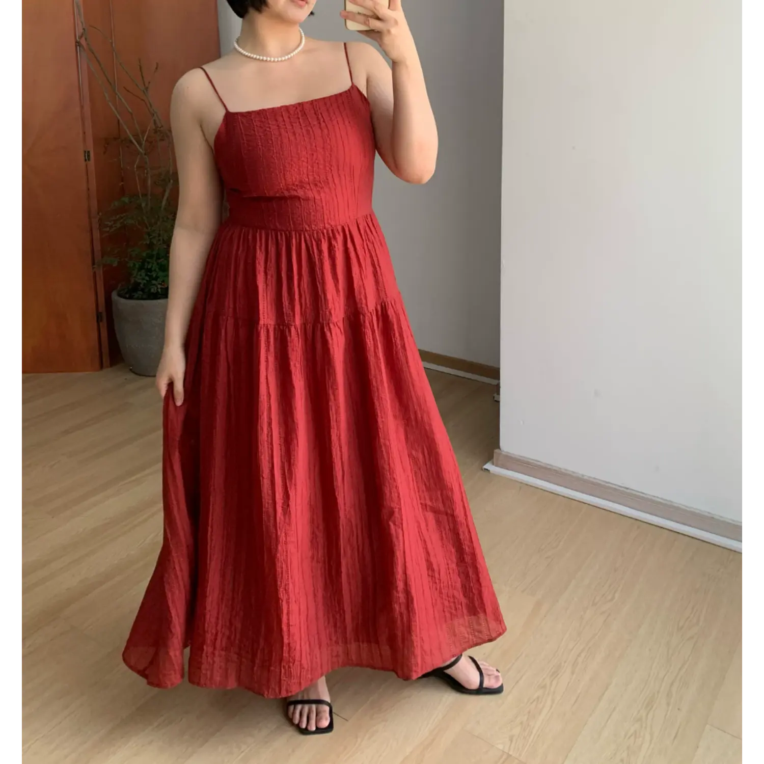 Indoor mirror full shot of deep red textured tiered slip maxi dress, thin adjustable straps, square neck, model lifting skirt hem to show lightweight crinkled fabric, black square toe slide sandals