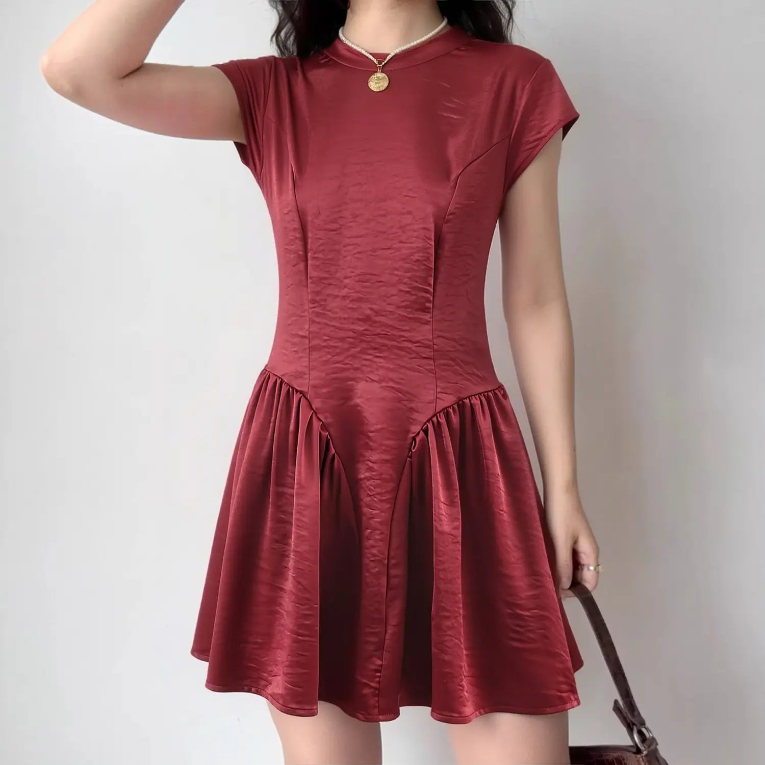 Model daily shot of wine red textured satin mini dress, slim mock neck cap sleeve, contour darted fitted waist, V-shaped gathered flared skirt, styled with double pearl & coin pendant necklace, vintage brown shoulder bag, romantic date night outfit
