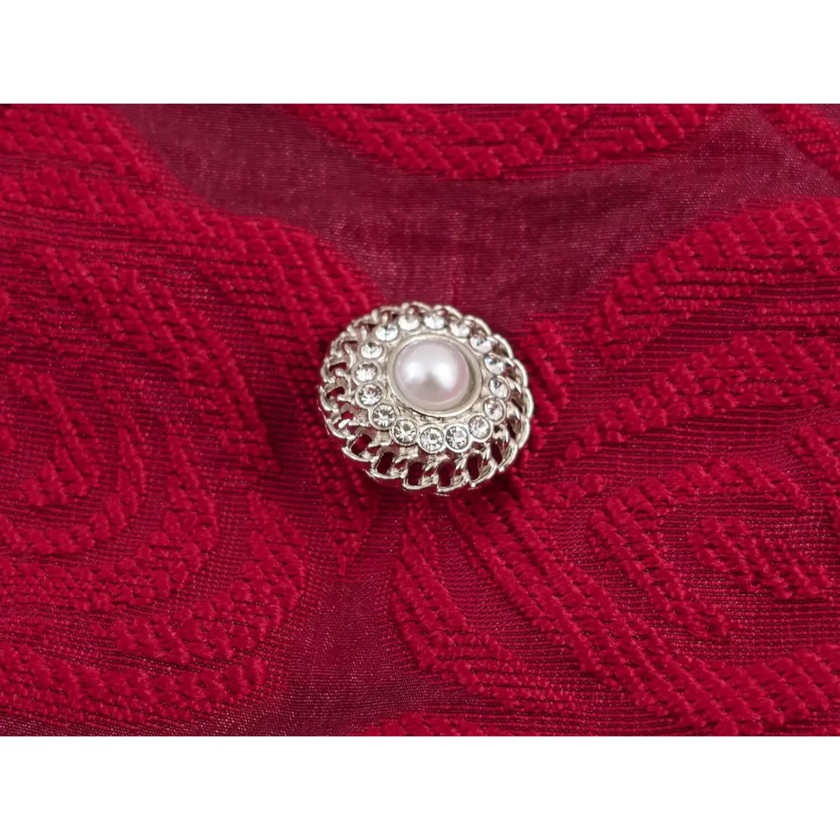 Close‑up of decorative pearl button on burgundy red jacquard fabric
