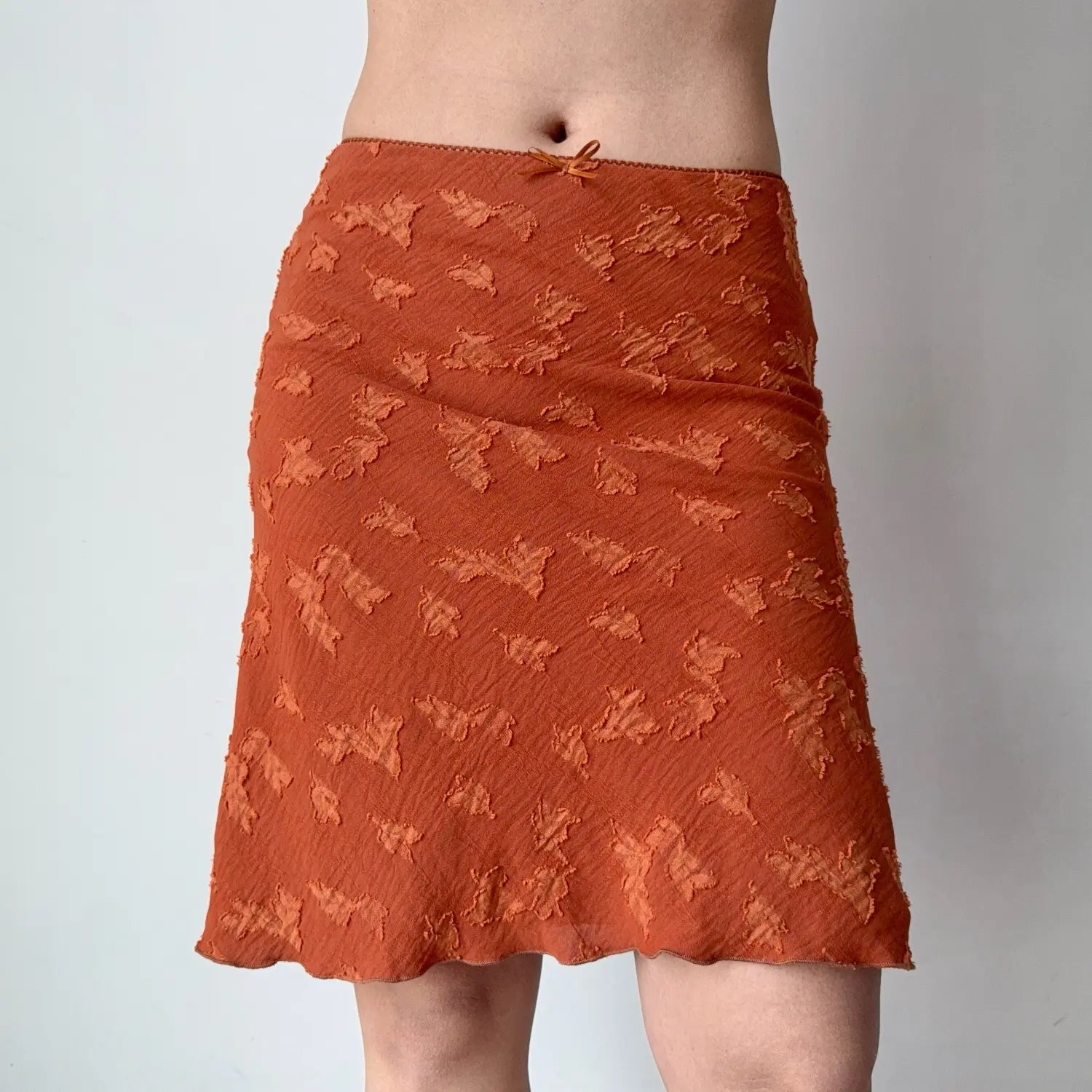 Front lifestyle shot on model of burnt orange embossed floral midi skirt, high waist fitted hip, soft flared wavy hem