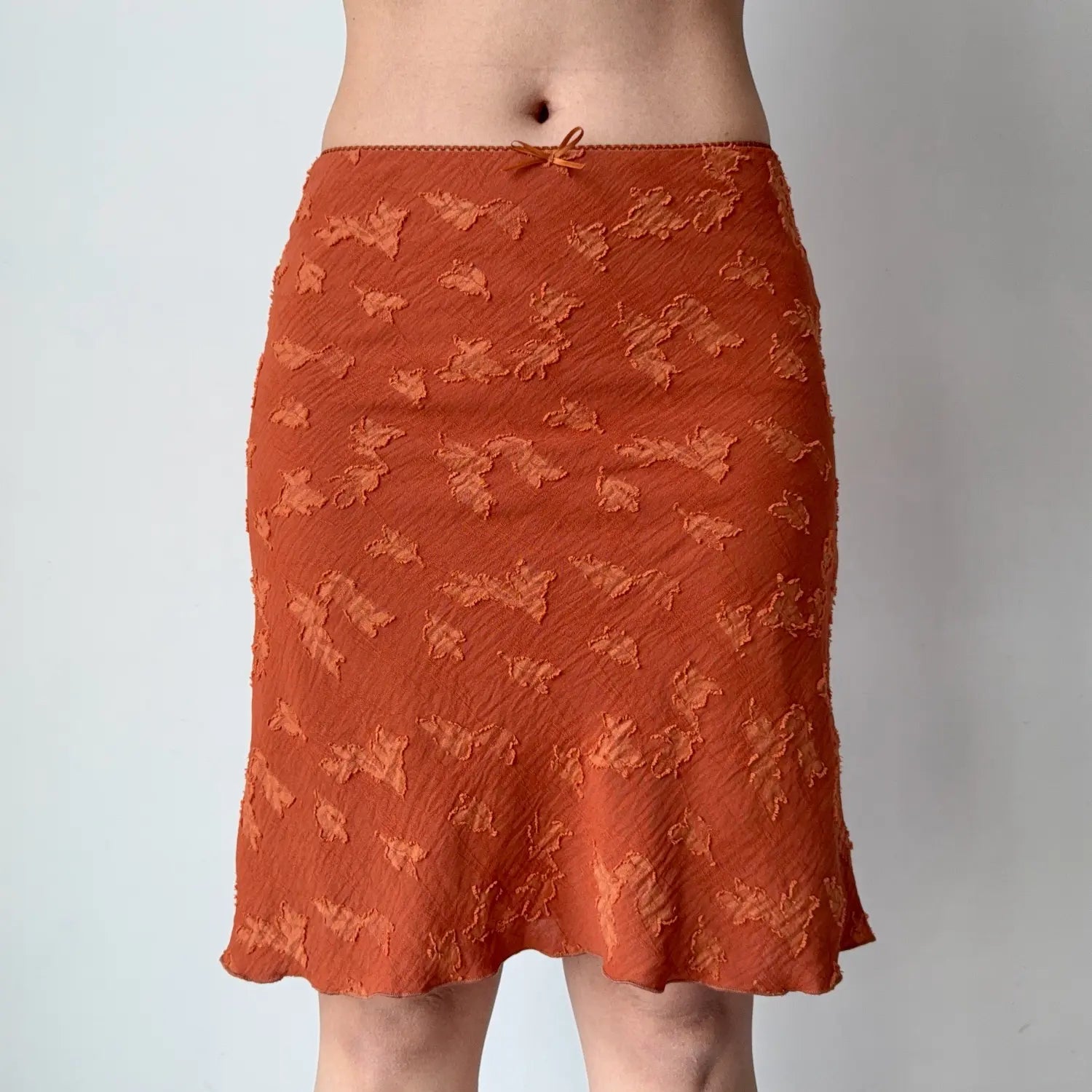 Front shot of burnt orange embossed floral midi skirt, tiny front bow detail, high waist, casual wavy hem flare skirt