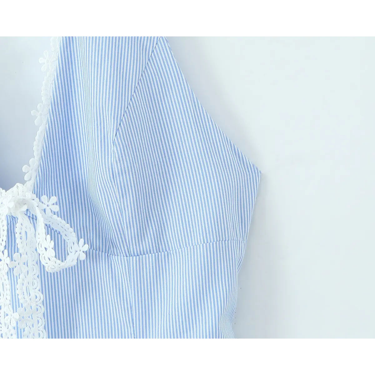 Close-up of the bust area on a blue and white striped halter dress, highlighting the V-neck and lace trim construction.