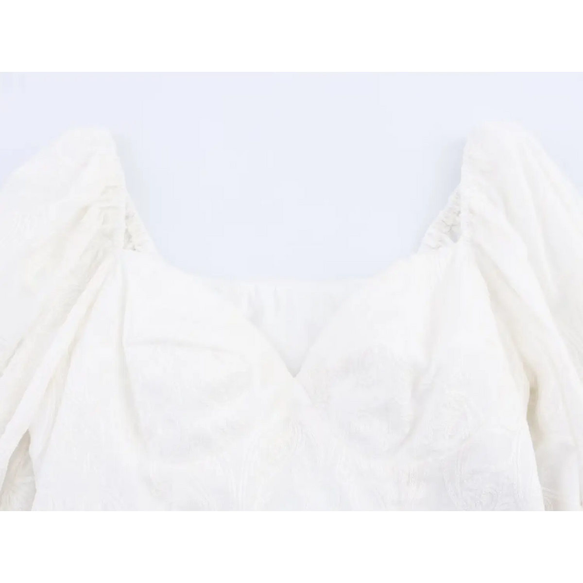 Close-up of bust area, v-shaped neckline with paisley embossed embroidery on white woven crop top