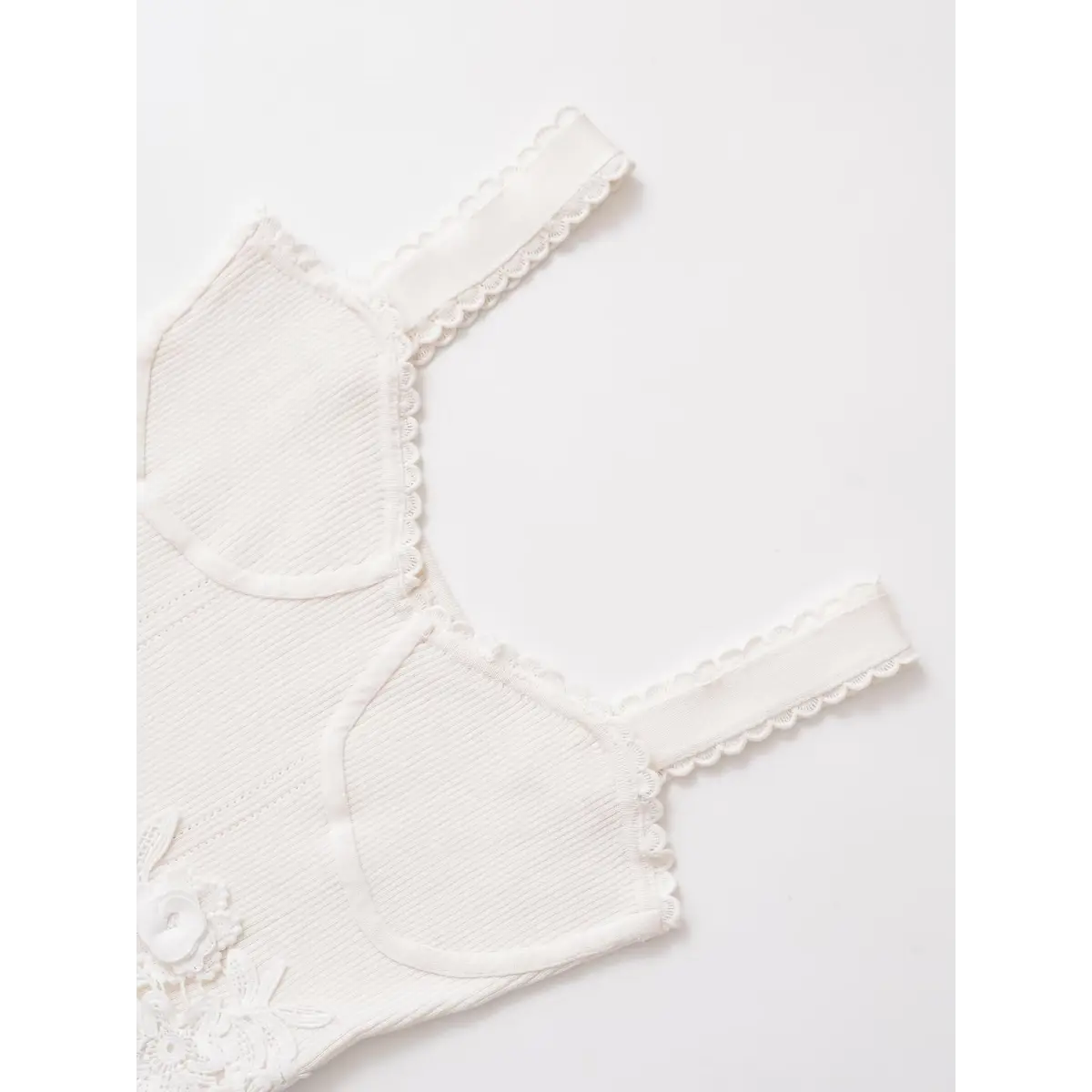 Close-up of the bustier-style seams and floral lace appliqu on a white ribbed cami top.