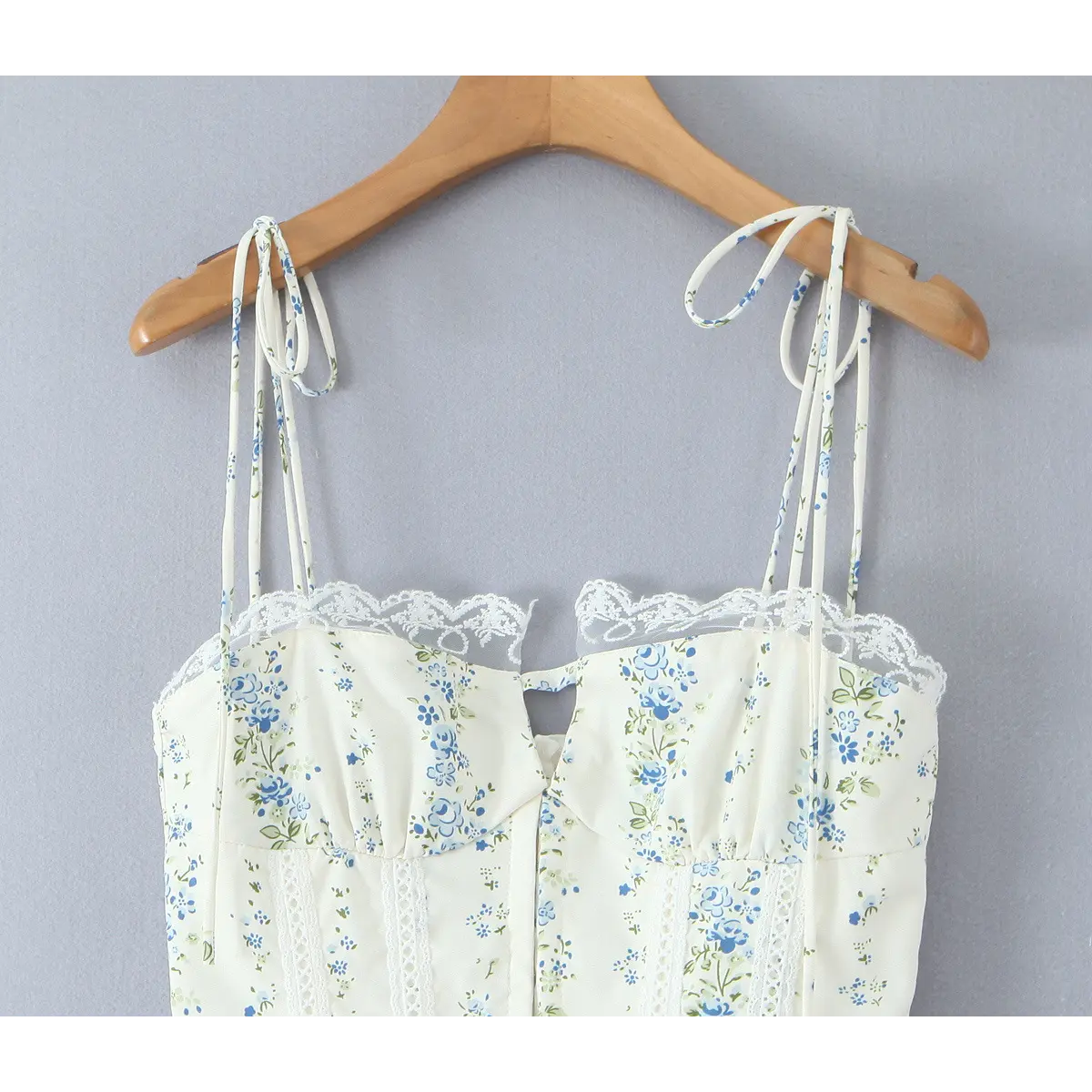 Close-up of the bustier-style bodice, scalloped lace trim, and tie straps on a cream floral dress.