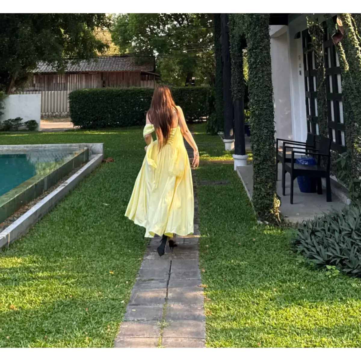 Back view of a woman in a butter yellow strapless bow dress walking away, revealing the corset lace-up closure and flowing skirt.