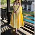 Woman in a butter yellow strapless bow-front dress by a pool, styled with a matching sheer shawl and black heels.