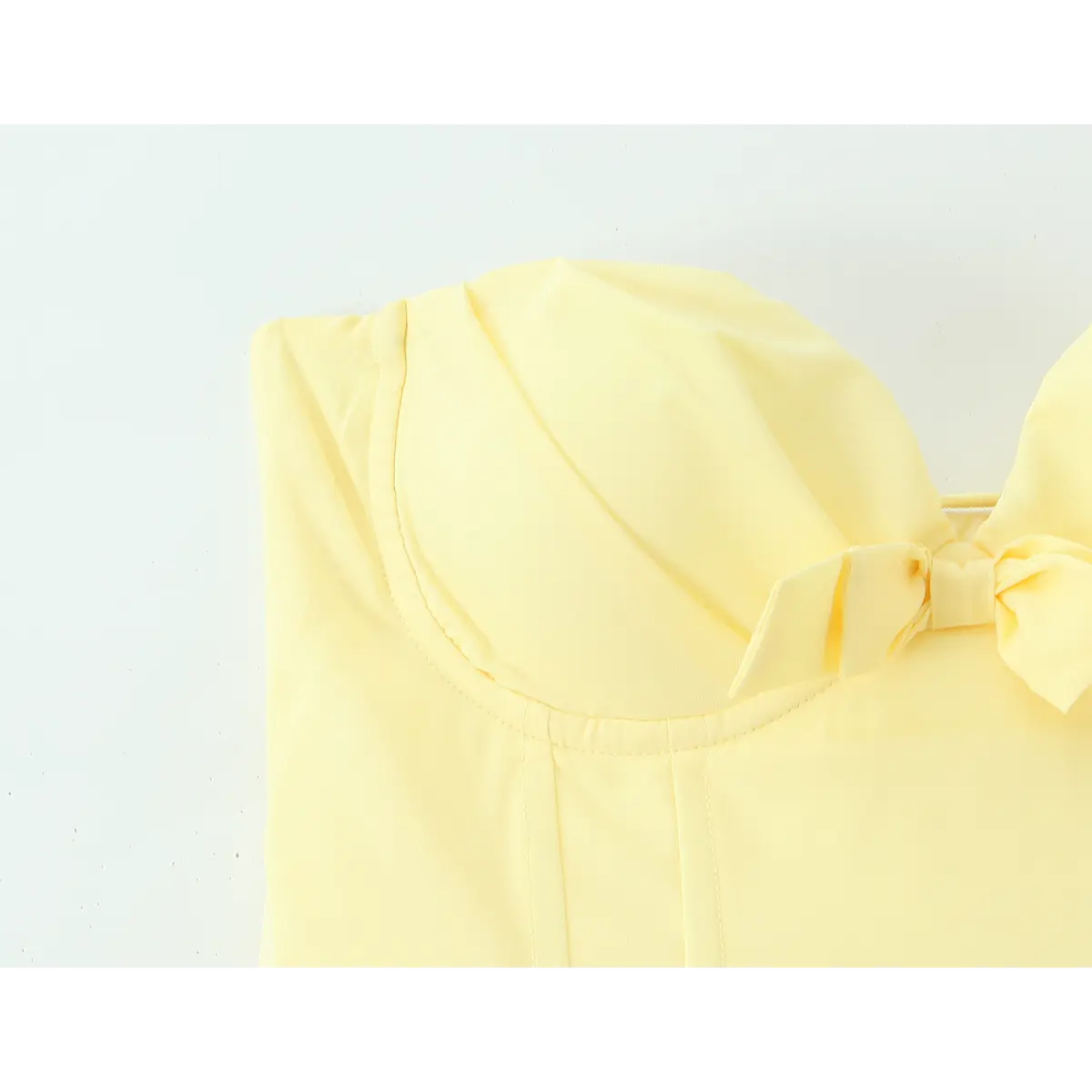 Close-up of the front bodice of a butter yellow strapless dress, highlighting the sweetheart neckline and decorative bow.