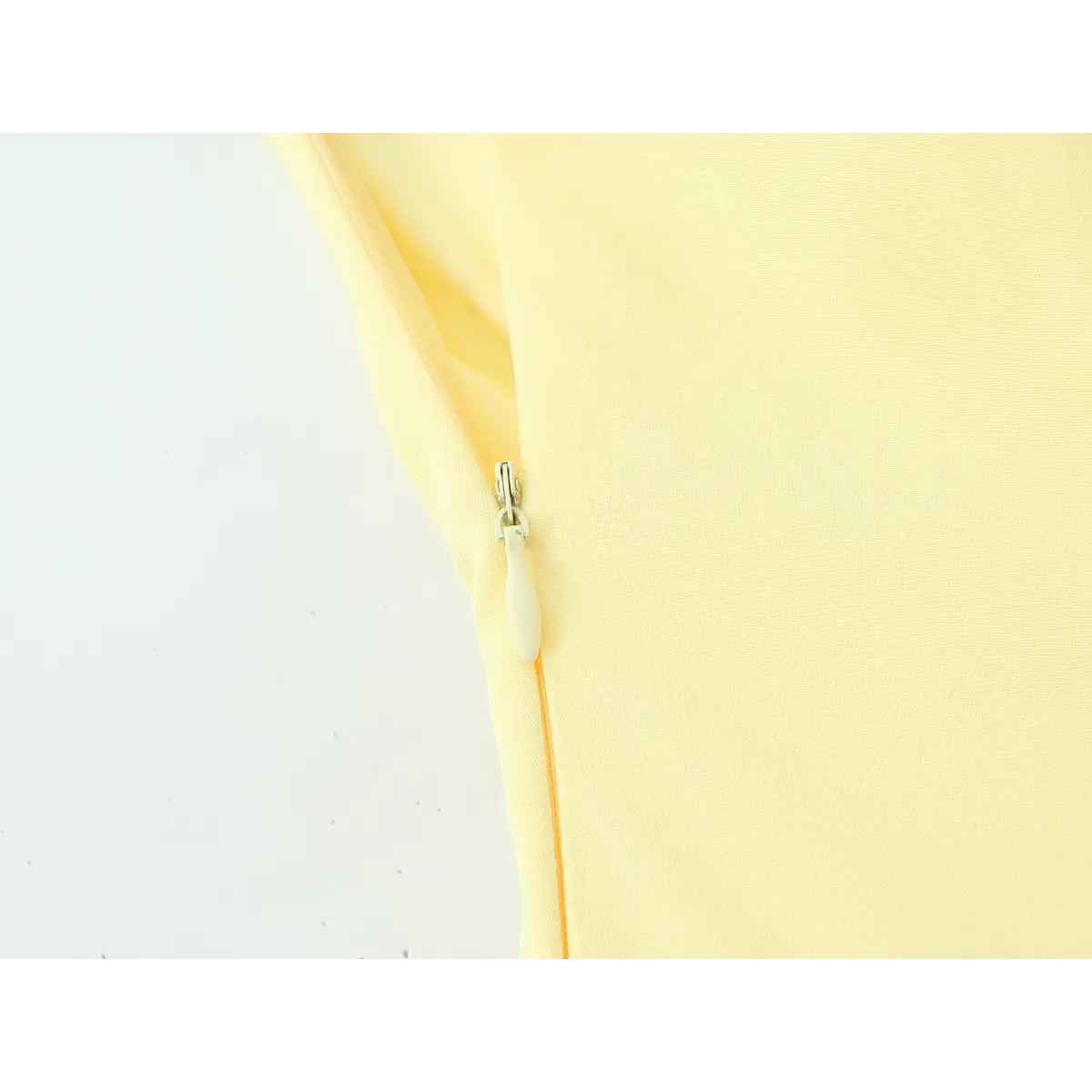  Close-up of the invisible side zipper on a butter yellow strapless dress, showing the light-colored pull tab.