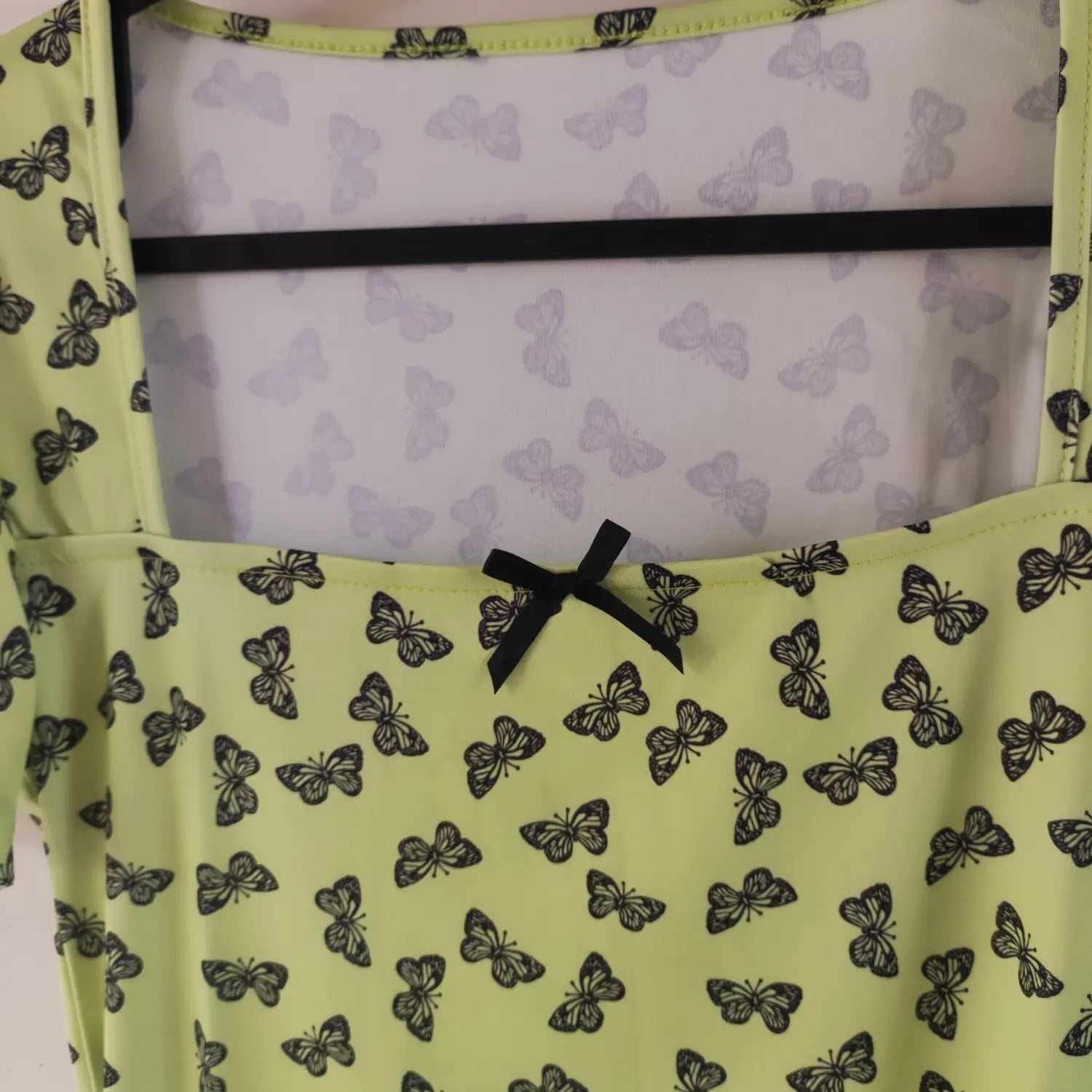 Close‑up square neckline, inner lining and small black bow ornament detail lime green butterfly print mini dress
